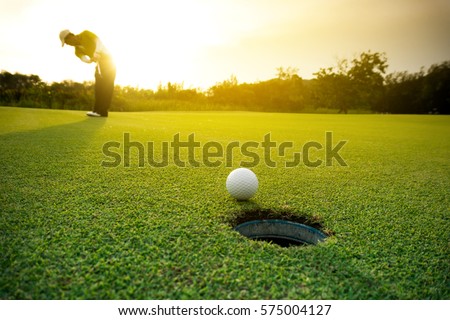 Golfer putting golf ball on the green golf, lens flare on sun set evening time. Royalty-Free Stock Photo #575004127