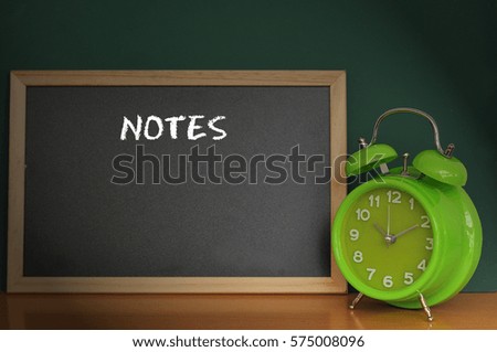 Vintage alarm clock and a blackboard with word NOTES on it background. Time management, business and financial concept.