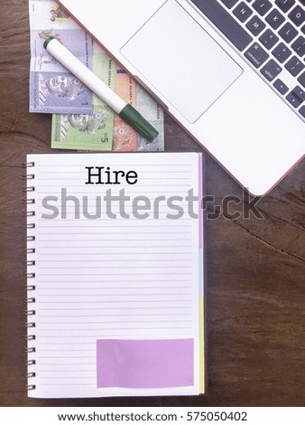 Hire : Winspiration Typed Words for Banking and Finance on a handbook with note book, marker pen and Malaysian Ringgit notes. Vertical view, Vintage and classic mood on the top of the wooden table.