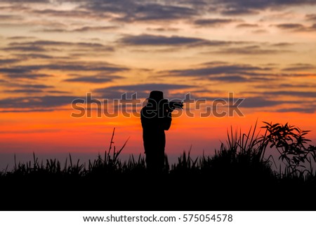 Cameraman silhouette on sunrise with orange light and clouds on the sky, on top of Thailand mountain.