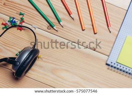 headphones colored pencils, markers, business card holder on a wooden background.
