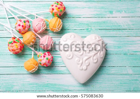 Bright cake pops  and white heart on turquoise  painted wooden background. Selective focus.