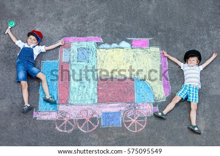 Two little kids boys having fun with train or steam locomotive picture drawing with colorful chalks on ground. Children, lifestyle, fun concept. funny friends playing and dreaming of future profession