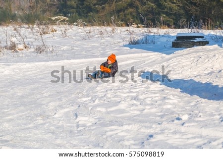 Happy little caucasian boy downhill on plastic slider or sledge. Winter child outdoor activity.
