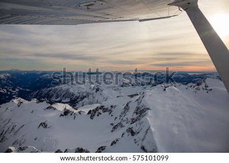 Looking out the window airplane while flying around the beautiful mountains of British Columbia, Canada. Picture taken North of Vancouver, BC, during a cloudy winter evening.