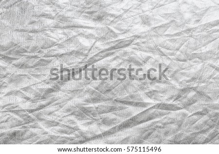 Thin textured sheet of silver leaf background with shiny uneven surface.
