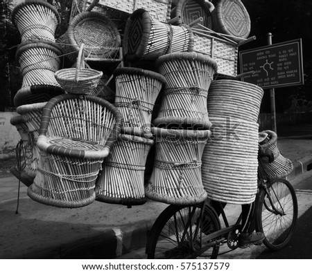 Hidden cyclist in Delhi riding a bike dangerously on road overloaded with wicker baskets Royalty-Free Stock Photo #575137579
