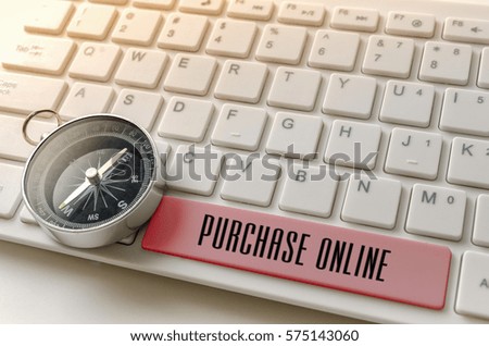 Close up of compass and word PURCHASE ONLINE on white keyboard.