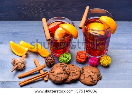 chocolate cookies with hot drink of mulled wine or tea with cinnamon spice stick in glass near christmas fir, decorative ball, orange fruit and pinecone on grey wooden background