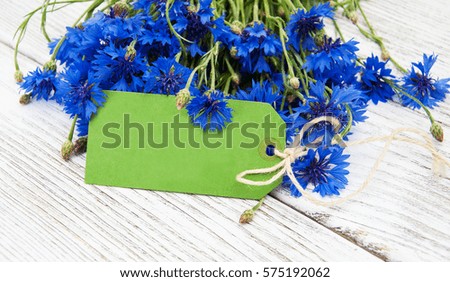 paper tag with blue fresh cornflowers on wooden table