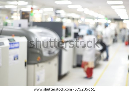 Workers working in SMT line of Electronics manufacturing company. Electronics production plant theme creative abstract blur background with bokeh effect, workers working on machines. Royalty-Free Stock Photo #575205661