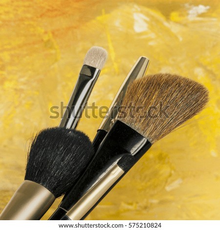 Makeup brushes on a blurred golden yellow background. A square template for a makeup artist's business card or flyer design, with copy space