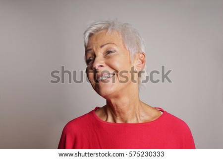 happy older woman with trendy short white hair laughing. gray background with copy space.