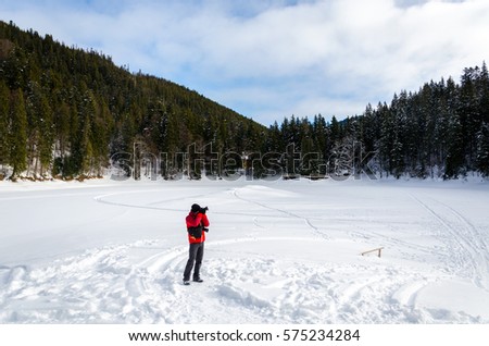A photographer takes pictures winter mountain landscape. snow field with trees covered with snow in the background