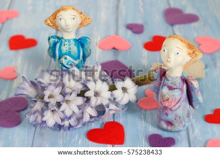 Two ceramic clay angels near hyacinth flower and hearts on shabby blue wooden planks in rustic style. 
