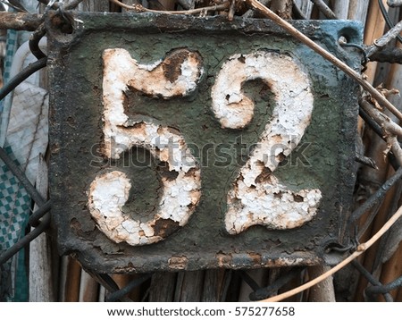 Vintage grunge square metal rusty plate of number of street address with number 52 closeup