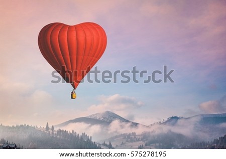 Red air balloon heart shape against blue and pink pastel sky in a sunny bright morning. Foggy mountains in the background. Romantic postcard background on Valentine's Day. Travel and recreation theme
