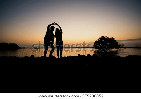 Soft focus silhouette of couple handmade heart-shaped with beautiful twilight lake scene 