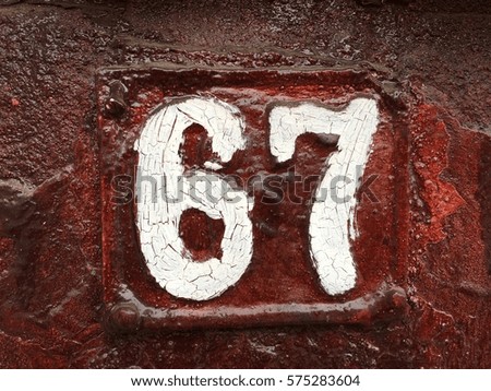 Vintage grunge square metal rusty plate of number of street address with number 67 closeup