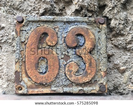 Vintage grunge square metal rusty plate of number of street address with number 63 closeup