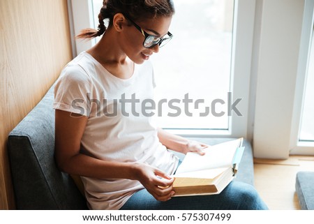 Photo of young african woman sitting in library and reading books.