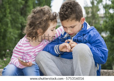 Summer in the park a little curly-haired boy shows his bad arm a little sister. She hugged him. Empathy regret it. Royalty-Free Stock Photo #575316016