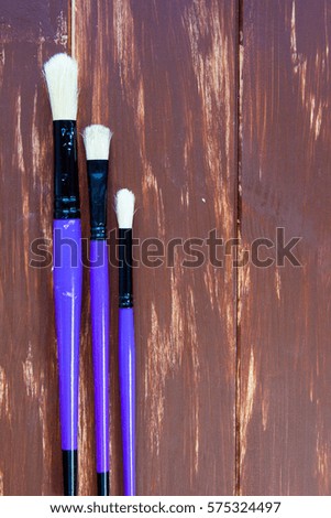 Three violet brushes (tools fro painting) at wooden background