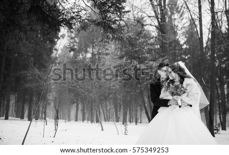 Young stylish wedding couple at forest on winter day. Loving newlyweds on snowy weather. Black and white photo. 