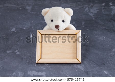 White teddy bear holding empty wooden frame. Gray background.