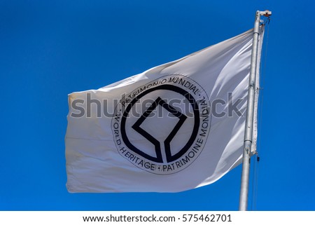 Flag of UNESCO World Heritage Committee waving in the wind at flagpole on the background of clear blue sky at sunny summer day