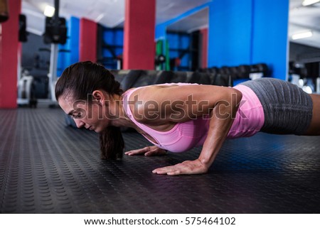 Side view of athlete woman doing push-ups in gym
