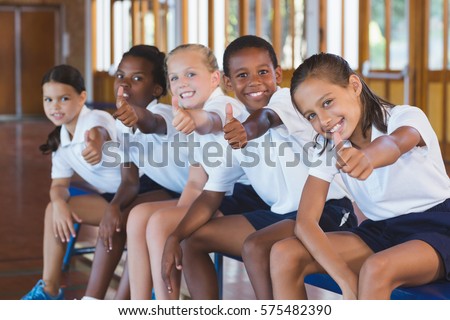 Portrait of school kids showing thumbs up in basketball court at school