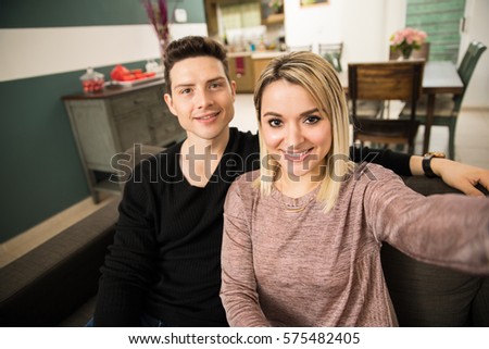 Wide angle view of a cute young couple taking a selfie at home and smiling