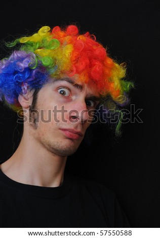 A silly crazy man wearing a clown wig with rainbow colors staring at the camera with a serious look.