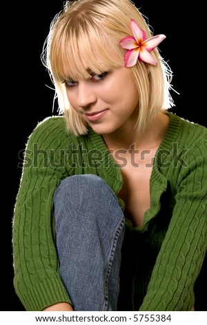 Cute young blond hair blue eyes woman wearing casual green sweater with a flower in her hair on dark background
