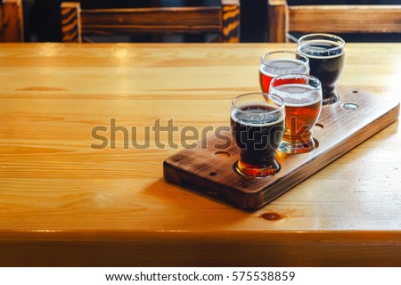 Flight with various types of craft beer in small glasses on a wooden table in a pub Royalty-Free Stock Photo #575538859