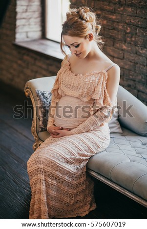 A young pregnant woman in a beautiful dress is sitting on the couch of a house that is being renovated.