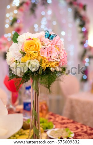 Bright festive bouquet in a tall vase with a decorative butterfly on the holiday table