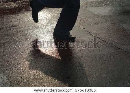 Unknown, unrecognizable  running person crossing the street.
Legs shadow, pedestrian, zebra crossing and wet red street after rain at sunset.
City life concept image. Back light.