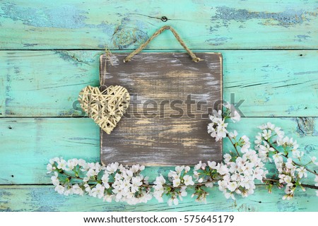 Welcome sign hanging on teal blue and mint green antique rustic wood background with  spring flowers border and wicker heart; springtime, Valentines Day, Mothers Day or love concept background