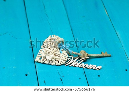 House key attached to natural wicker heart with ribbon and Welcome on antique rustic teal blue wood background; new home, Valentines Day, love and welcome home  background with painted copy space