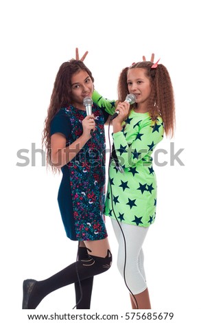 Two young girls girlfriends with long hair singing into two microphones on a white background