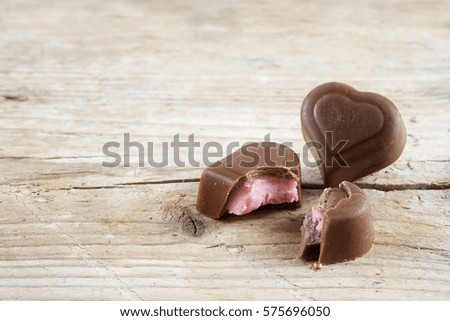 Two filled chocolate hearts, one broken, on bright rustic wood for valentine's or mothers day, close up, selected focus,  narrow depth of field