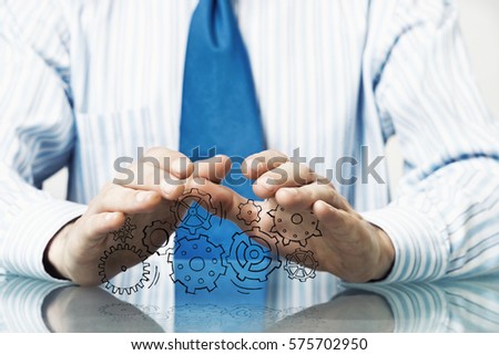 Close up of businessman sitting at table and showing gear mechanism in palms