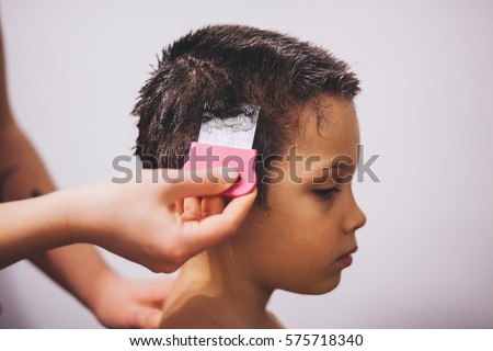 Profile pose of a hand doing treatment on a boy's hair with lice 