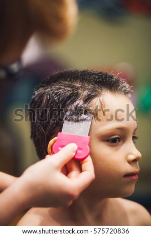 Close-up of doctor's hand doing treatment on boy's hair with comb
