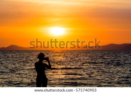 silhouette woman use camera phone take picture on the beach at sunset over sea background. Blur photo