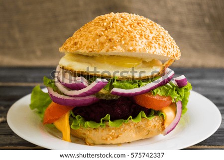 Hamburger with fried eggs and beetroot on a wooden table and ingredients