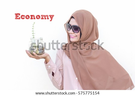 Image of Asian women holding a glass jar with coins inside, growing tree and Economy words typed. Conceptual image focus on women investment, business, finance and financial planning.