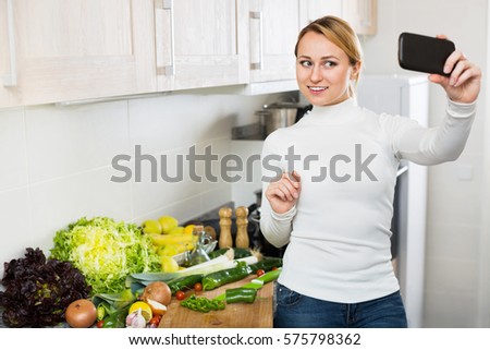 Cheerful smiling housewife making photo of herself with smartphone in hand 